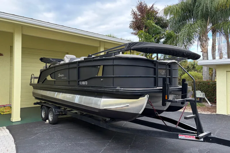 The Image of 2022 Barletta Lusso 23QCSS pontoon boat on trailer, parked near a garage. - 0