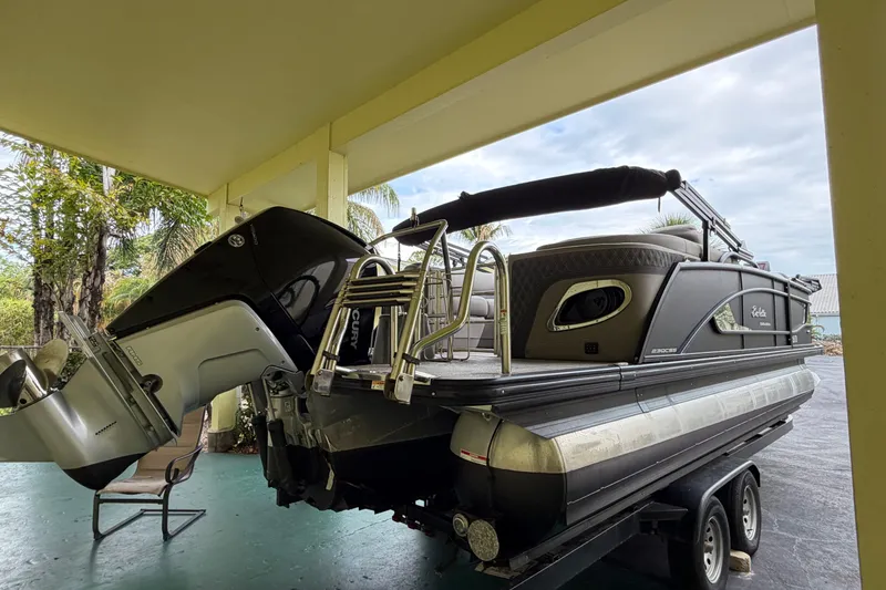 Slide: The Image of 2022 Barletta Lusso 23QCSS pontoon boat on trailer under a covered area. - 4