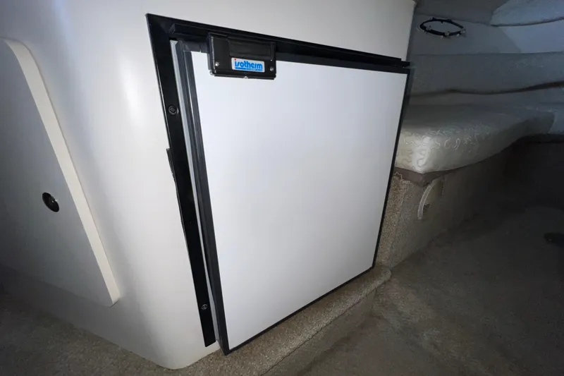 Slide: The Image of Built-in fridge inside 2002 Larson Cabrio 254 boat cabin, featuring compact design and white door. - 16