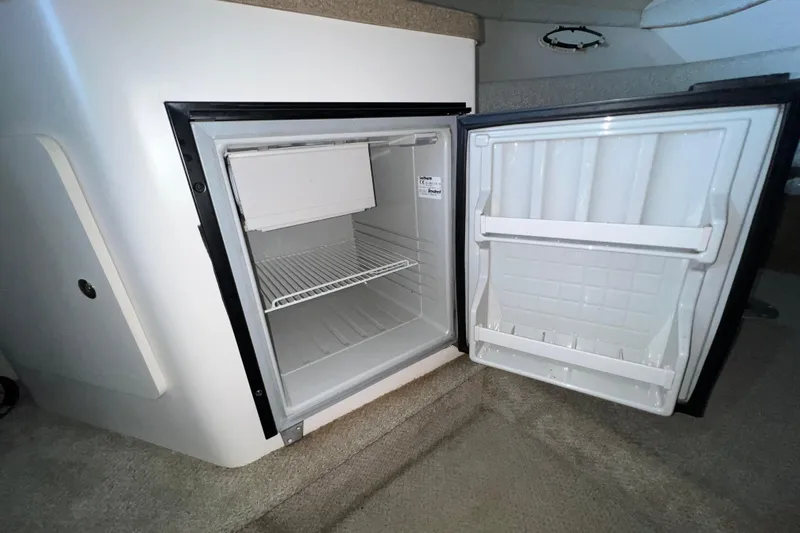 Slide: The Image of Open refrigerator inside 2002 Larson Cabrio 254 boat cabin, showcasing interior storage space. - 17