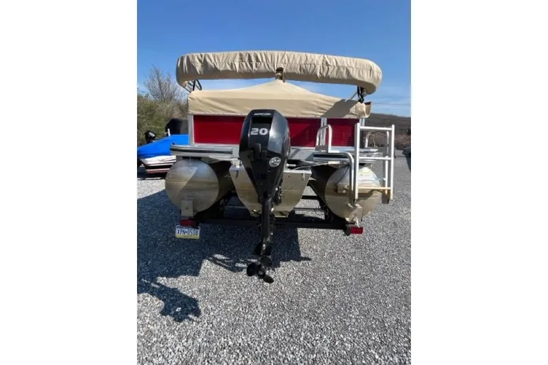 Slide: The Image of 2023 Lowe Ultra 200 Cruise pontoon boat with outboard motor, parked on gravel. - 2