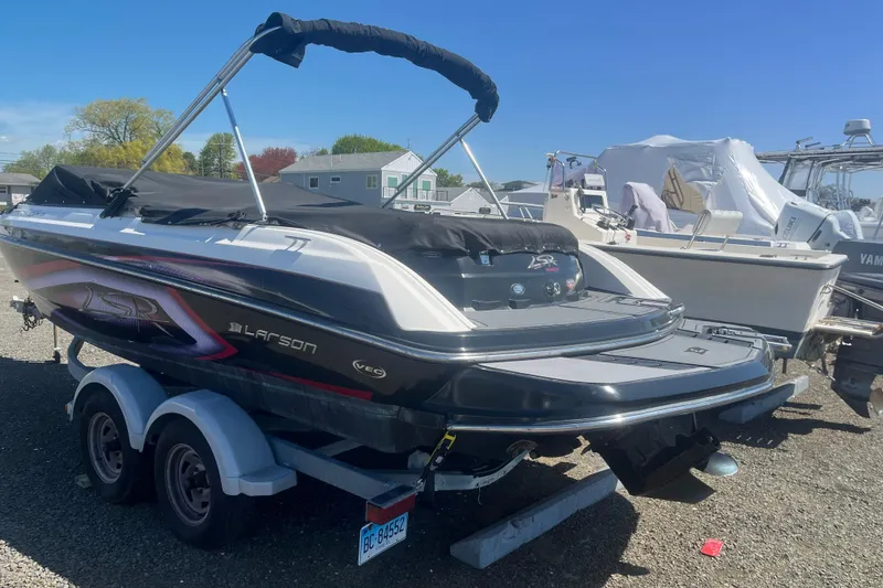 Slide: The Image of 2013 Larson LSR 2300 I/O boat on trailer, parked outdoors under clear blue sky. - 2