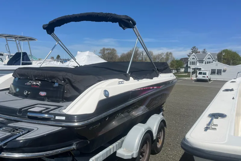 Slide: The Image of 2013 Larson LSR 2300 I/O boat on trailer, parked outdoors under clear blue sky. - 3