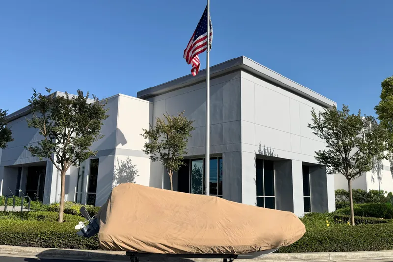 Slide: The Image of 2021 Novurania Deluxe 335 boat covered, parked outside modern building with American flag. - 26