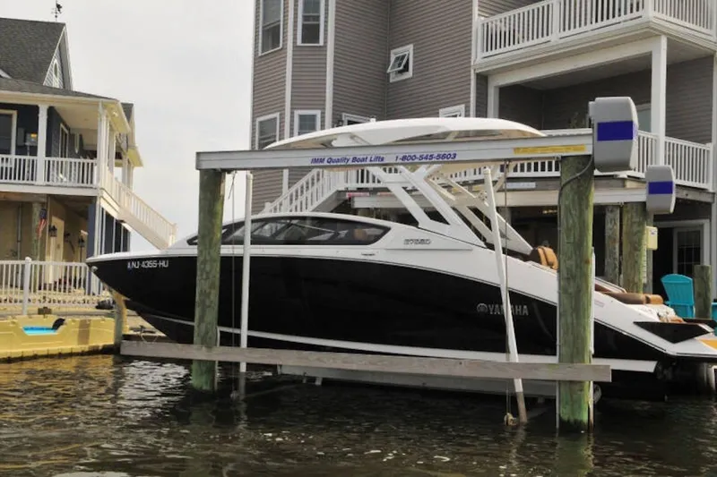The Image of 2024 Yamaha Boats 275SDX on a lift near waterfront homes. - 0