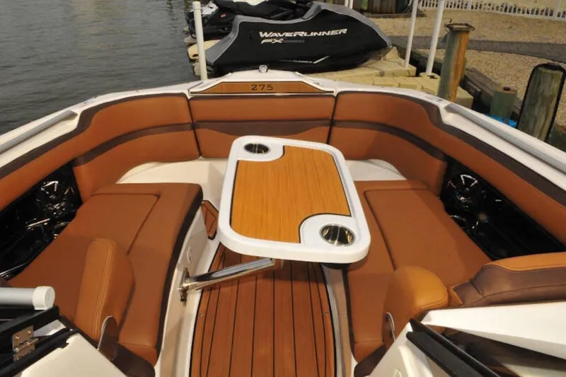 Slide: The Image of 2024 Yamaha Boats 275SDX interior with brown seating and wooden table, docked by the water. - 29