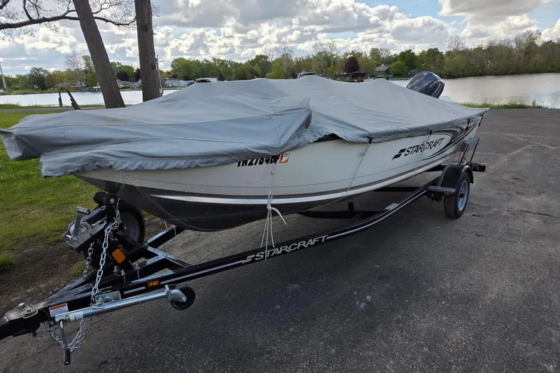 Slide: The Image of 2023 Starcraft Patriot 16 SC boat covered on trailer by a lake. - 3