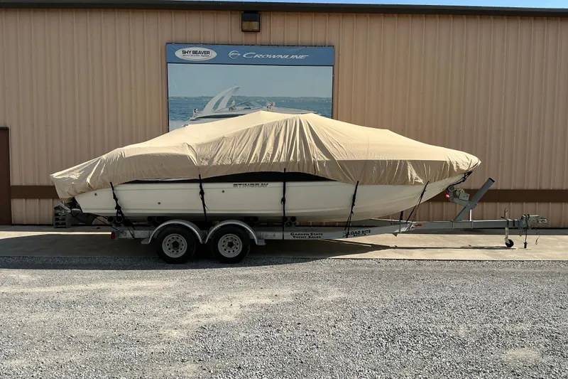Slide: The Image of 2010 Stingray 250 LR boat covered on trailer, parked outside a building. - 17