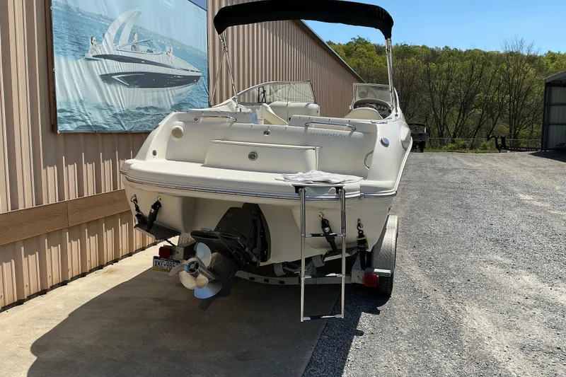 Slide: The Image of 2010 Stingray 250 LR boat on trailer, parked near a building with a marine poster. - 3