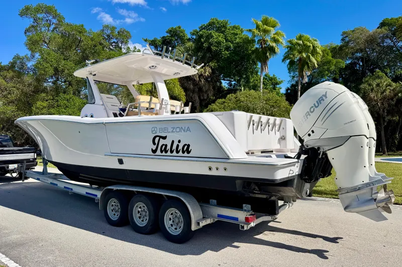 Slide: The Image of 2013 Belzona 32 CC boat on trailer with Mercury outboard, parked near lush greenery. - 10