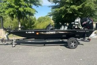 The Image of 2016 Lowe Stinger 180 boat on trailer, parked outdoors with trees in the background. - 1