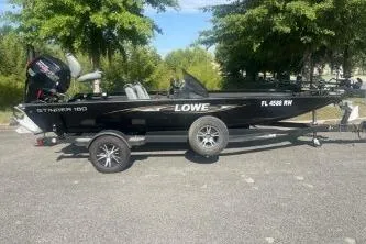 Slide: The Image of 2016 Lowe Stinger 180 boat on trailer, parked outdoors, surrounded by trees. - 9