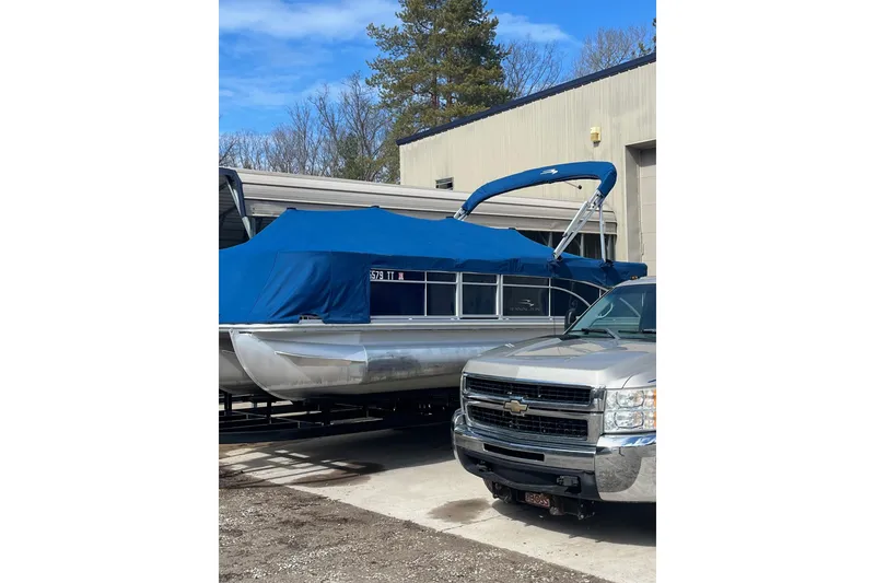 The Image of 2014 Bennington 22 SLX pontoon boat with blue cover, parked beside a Chevrolet truck. - 1