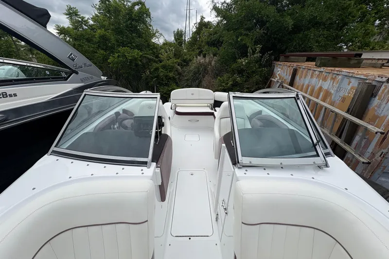 Slide: The Image of 2013 Cobalt 242 boat interior with white seating and dual windshields, parked outdoors. - 5