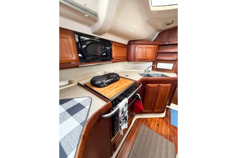 Slide: The Image of Hunter 430 yacht kitchen interior, featuring wooden cabinetry, stove, microwave, and sink, 1996 model. - 62