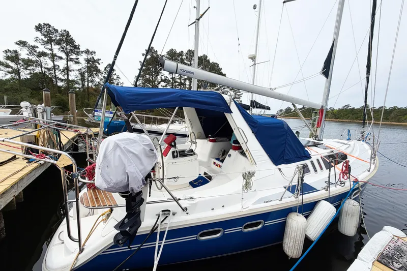 Slide: The Image of 1996 Hunter 430 sailboat docked, featuring blue canopy and white hull, surrounded by calm water. - 87