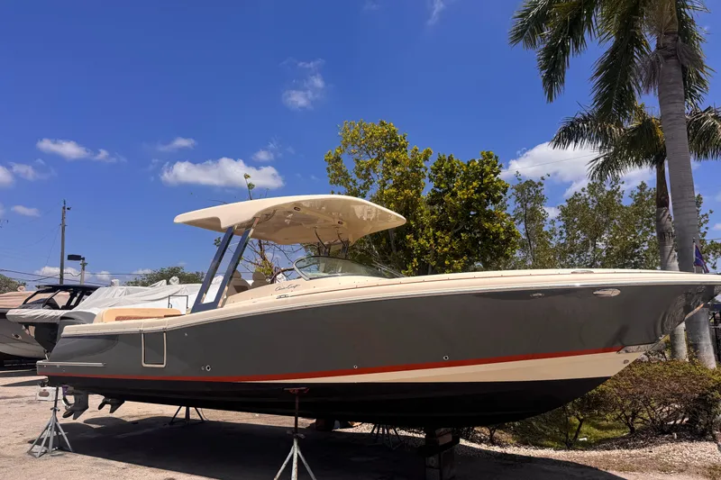 Slide: The Image of 2018 Chris-Craft Calypso 30 boat on stands, under clear blue sky with palm trees. - 18