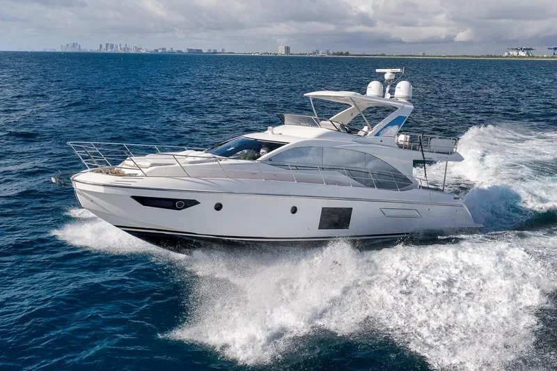 Slide: The Image of 2019 Azimut 55 yacht cruising on open ocean with city skyline in background. - 6