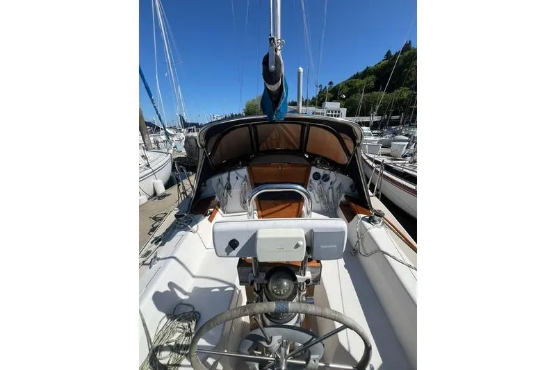 Slide: The Image of 1988 Catalina 30 sailboat cockpit with steering wheel, docked at marina under clear blue sky. - 10