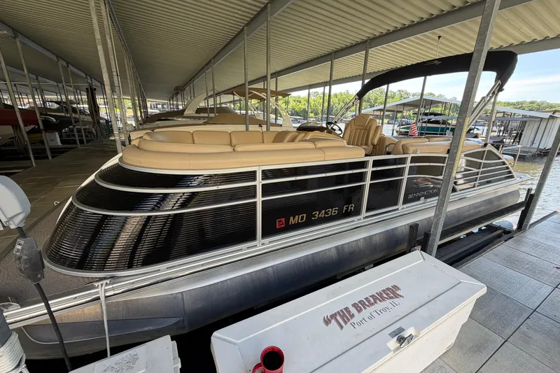 The Image of 2011 Bennington 2575QCW OB pontoon boat docked under a covered marina. - 0