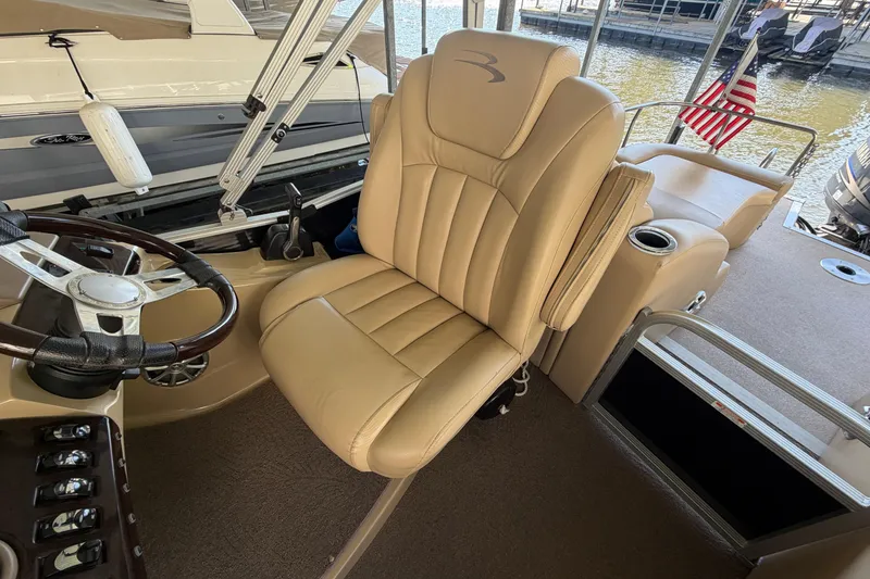 Slide: The Image of Captain's chair on 2011 Bennington 2575QCW OB pontoon boat, featuring beige upholstery and steering wheel. - 16