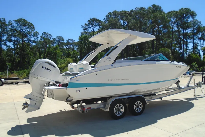 Slide: The Image of 2022 Regal LX6 boat with Yamaha engine on trailer, surrounded by trees. - 2