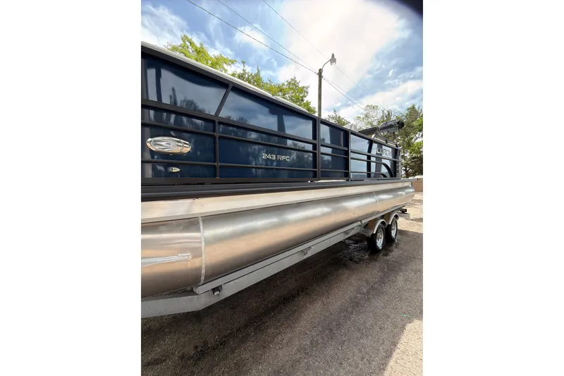 Slide: The Image of 2026 Coach 243 pontoon boat with sleek design and dual axles, parked outdoors. - 19