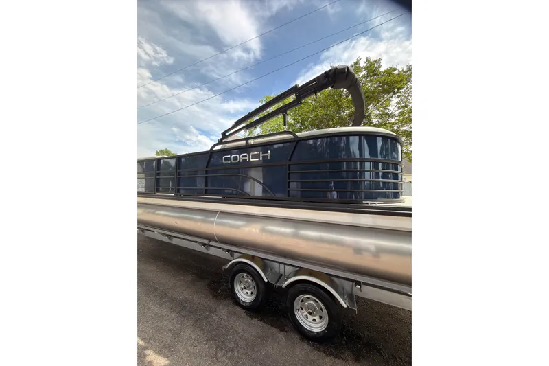 Slide: The Image of 2026 Coach 243 pontoon boat on trailer under a clear blue sky. - 3