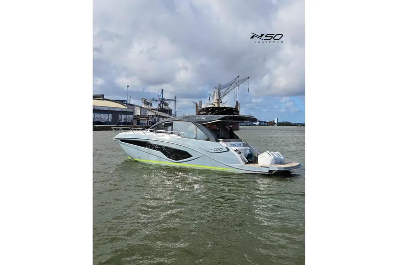 Slide: The Image of 2025 NX Boats NX50 Invictus HT yacht on water, industrial backdrop, cloudy sky. - 1