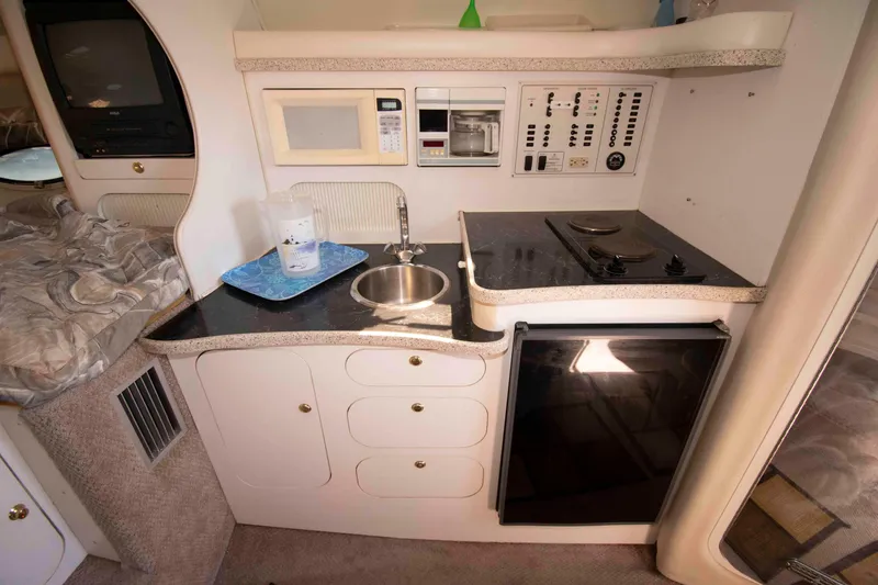 Slide: The Image of Compact kitchen area in a 2000 Rinker Fiesta Vee 310 boat, featuring stove, sink, and microwave. - 11