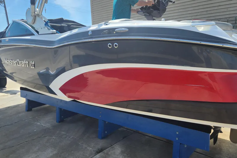 The Image of 2015 MasterCraft X23 boat with sleek red and gray design on a blue stand. - 1