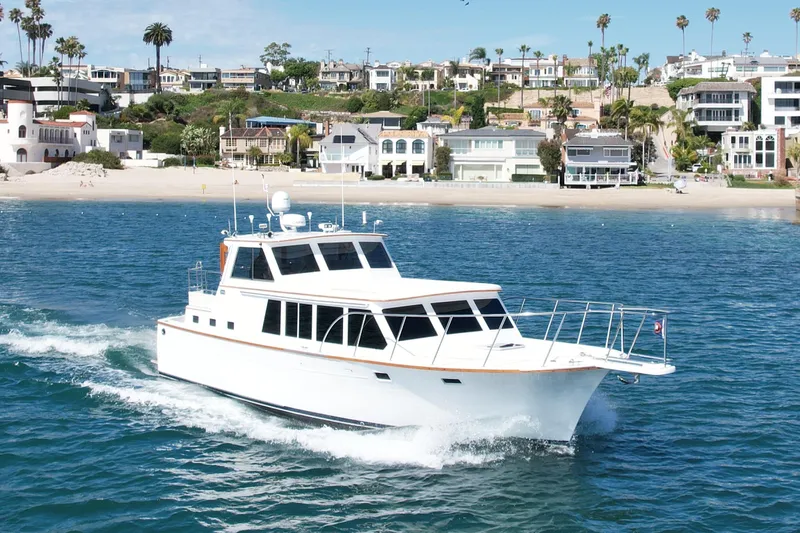 Slide: The Image of 1980 Roughwater 41 yacht cruising near a scenic coastal town with beachfront homes. - 2