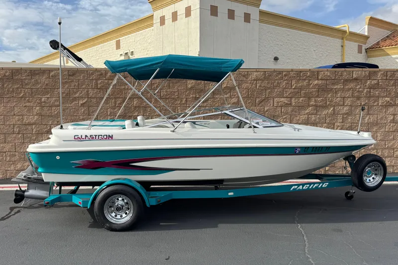 The Image of 1997 Glastron GS 185 boat on trailer with teal accents and canopy. - 0