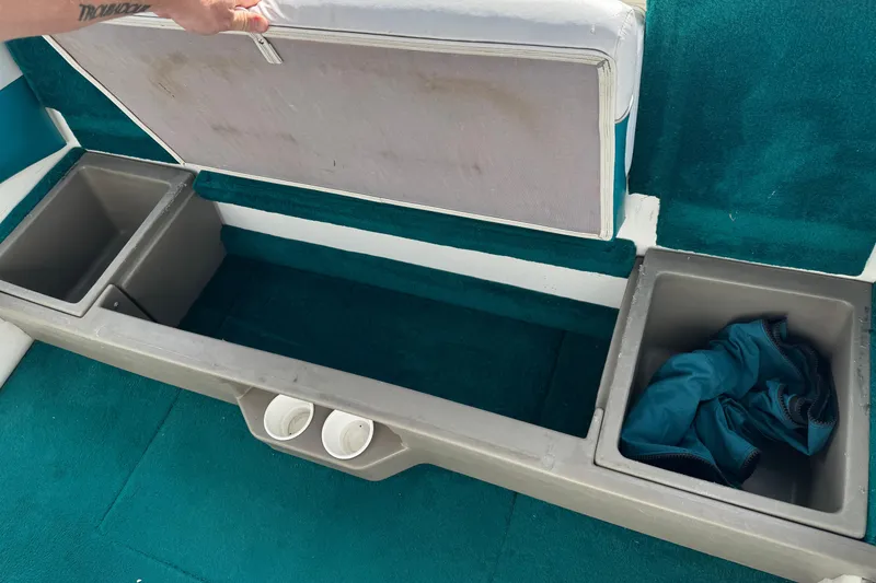 Slide: The Image of 1997 Glastron GS 185 boat interior storage compartments with teal carpet and cup holders. - 15