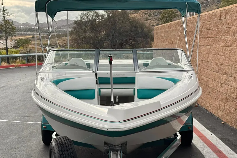 Slide: The Image of 1997 Glastron GS 185 boat with teal accents and canopy, parked on a trailer. - 2