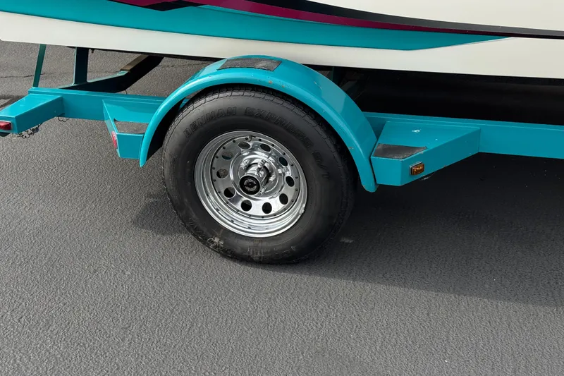 Slide: The Image of Teal trailer wheel of a 1997 Glastron GS 185 boat on asphalt. - 22