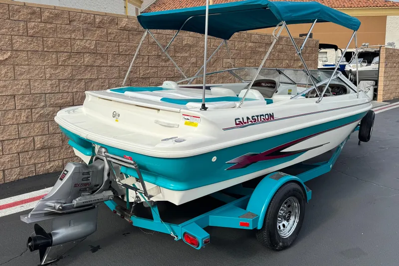 Slide: The Image of 1997 Glastron GS 185 boat with teal accents and trailer, parked outdoors. - 5