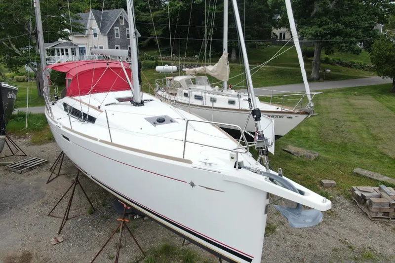 Slide: The Image of 2017 Jeanneau Sun Odyssey 389 sailboat on land, with red canopy, near houses and greenery. - 3