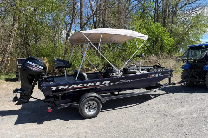 The Image of 2019 Bass Tracker Pro 17 boat with Mercury engine, parked on a trailer near trees. - 1