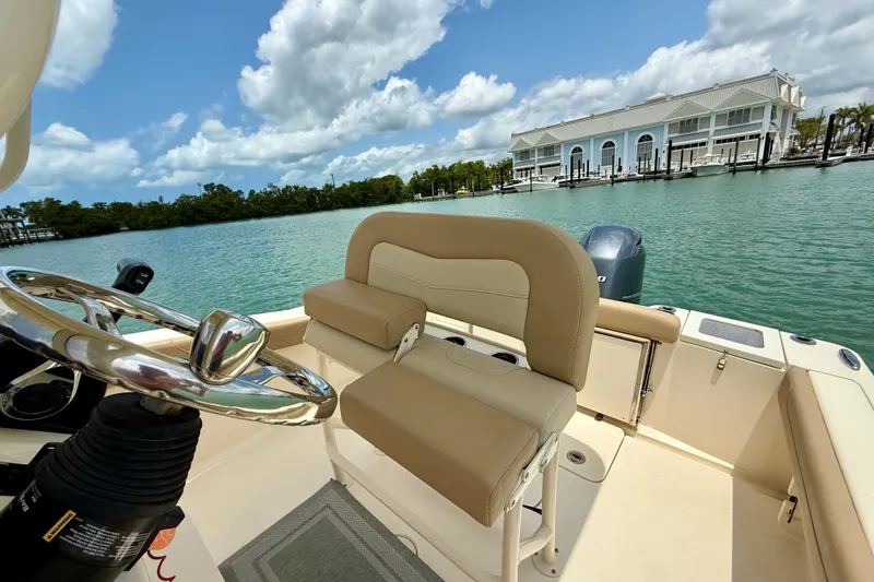 Slide: The Image of 2023 Scout 215 XSF boat interior with steering wheel, beige seating, and waterfront view. - 14