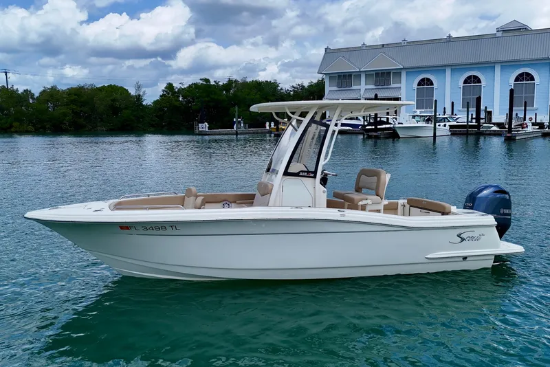 Slide: The Image of 2023 Scout 215 XSF boat on calm water near a marina, under a partly cloudy sky. - 8