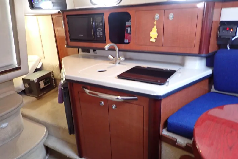 Slide: The Image of 2005 Sea Ray Sundancer 260 interior with kitchenette, featuring sink, microwave, and wooden cabinetry. - 98