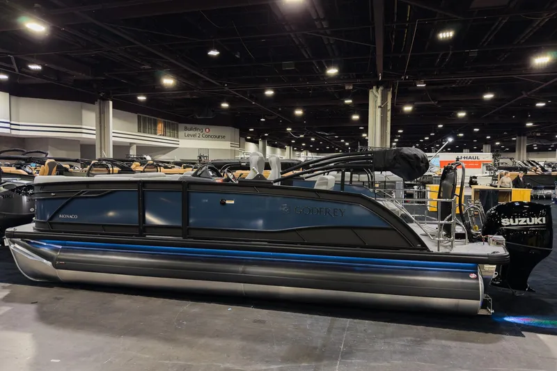 Slide: The Image of 2026 Godfrey Monaco 235 pontoon boat displayed indoors, featuring sleek design and Suzuki engine. - 2