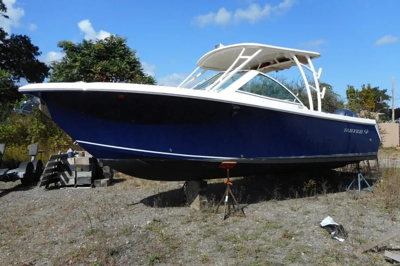 The Image of 2020 Sailfish 275 DC boat on land, blue hull, white top, clear sky background. - 1