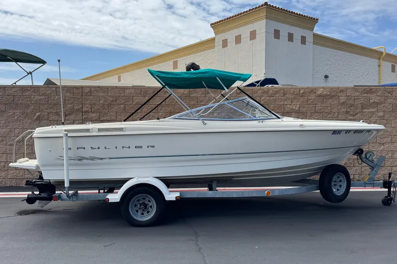 The Image of 2000 Bayliner 2150 Capri boat on trailer with green canopy, parked outdoors. - 0