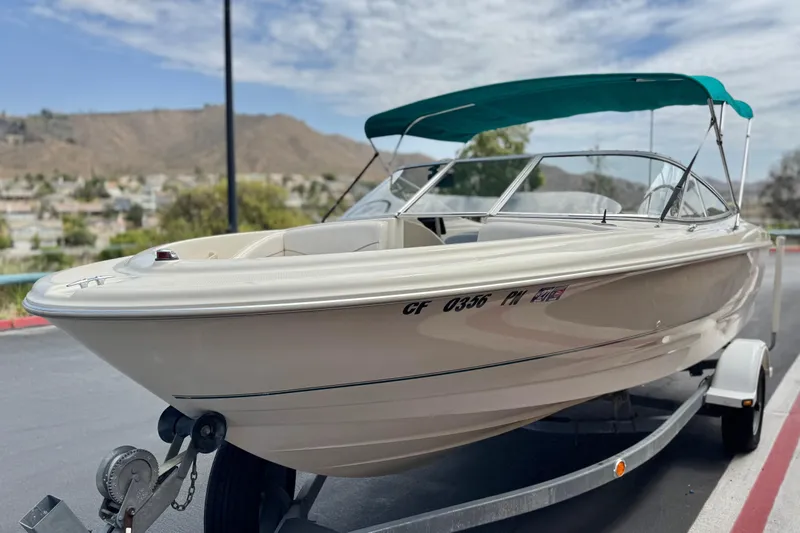 Slide: The Image of 2000 Bayliner 2150 Capri boat on trailer with teal canopy, scenic background. - 3