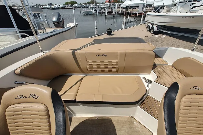 Slide: The Image of 2023 Sea Ray SPX 190 boat interior with tan leather seating and wood accents at a marina. - 21