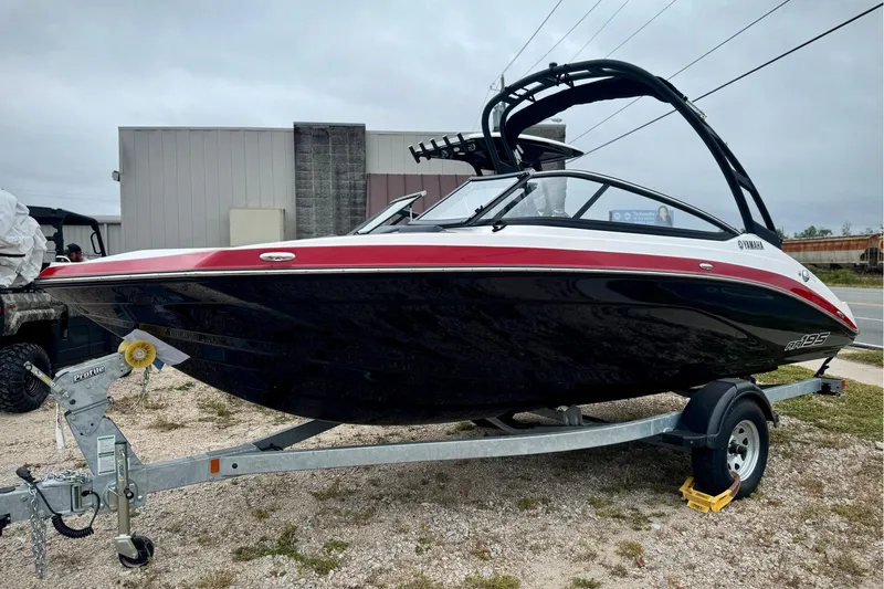 The Image of 2025 Yamaha Boats AR195 on trailer, sleek black and red design, parked outdoors. - 0