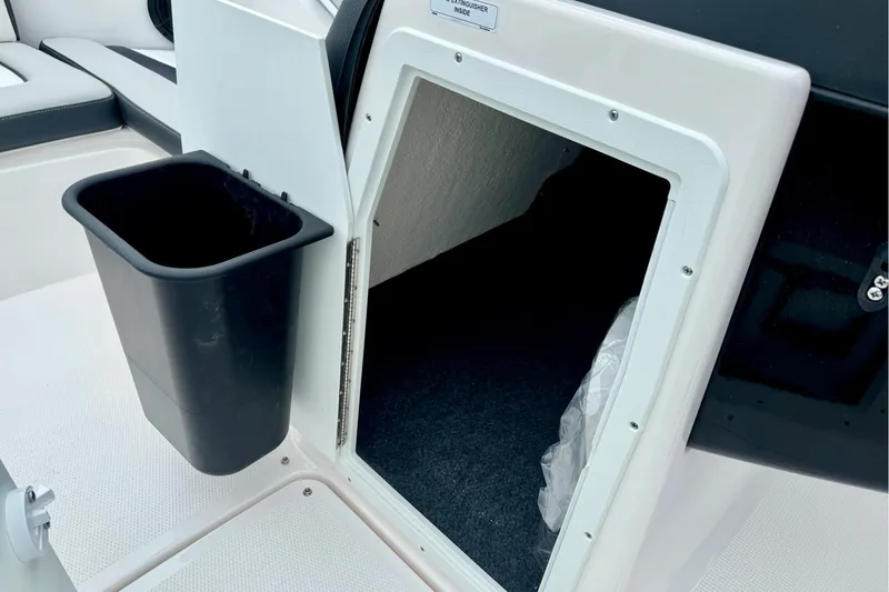 Slide: The Image of 2025 Yamaha Boats AR195 storage compartment with black trash bin on deck. - 28