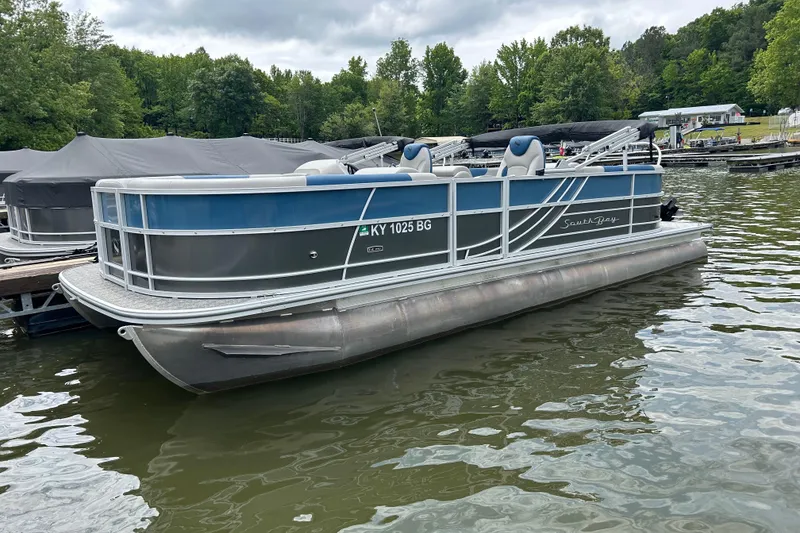 Slide: The Image of 2025 Southbay 224RSLE25 pontoon boat docked on a lake with lush greenery. - 23